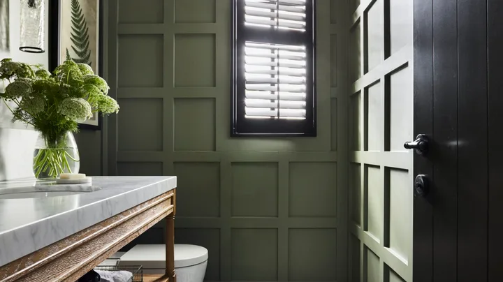 A forest green powder room with a mosaic tiled floor.