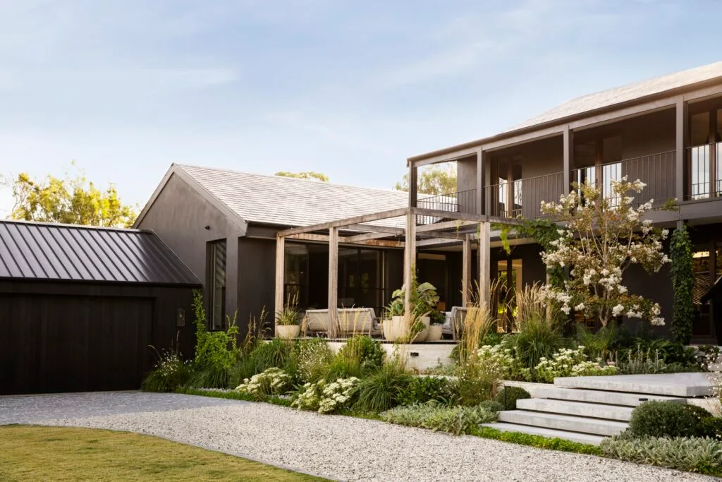 A modernist timber and steel two-storey home with sprawling white and green plant beds.