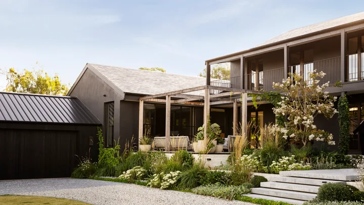 A modernist timber and steel two-storey home with sprawling white and green plant beds.