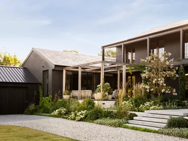 A modernist timber and steel two-storey home with sprawling white and green plant beds.