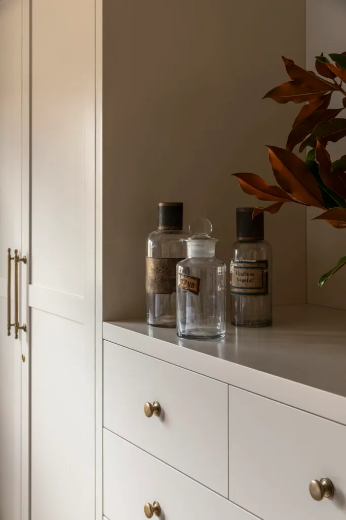 Glass bottles on top of in-built bedroom drawers.