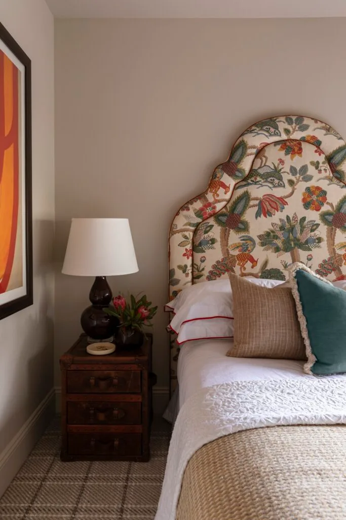 A bed with a floral patterned bedhead, timber side table and rounded lamp.