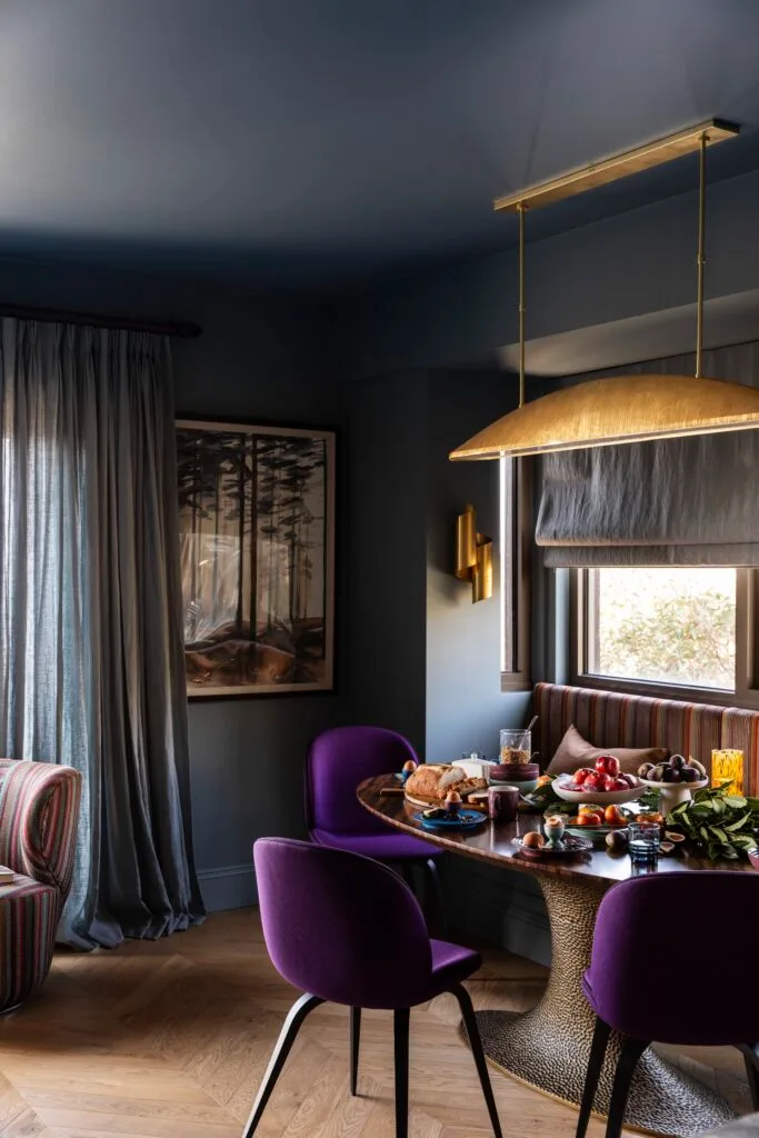 A dining nook with purple chairs beside a framed forest print.