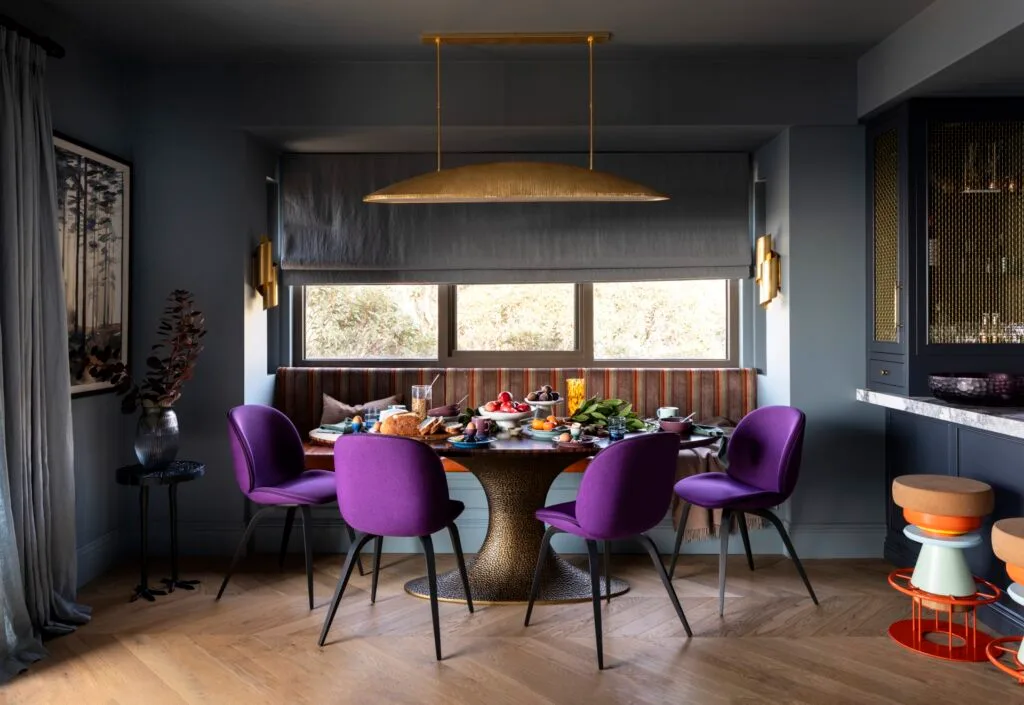 A dining nook with purple chairs, a mixed patterned bench seat and a brass pendant.