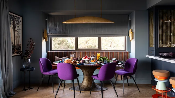 A dining nook with purple chairs, a mixed patterned bench seat and a brass pendant.