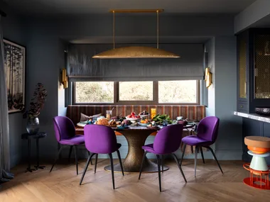 A dining nook with purple chairs, a mixed patterned bench seat and a brass pendant.