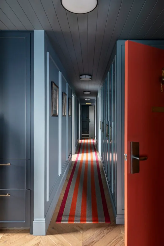 An apartment hallway in teal with an orange striped rug runner.