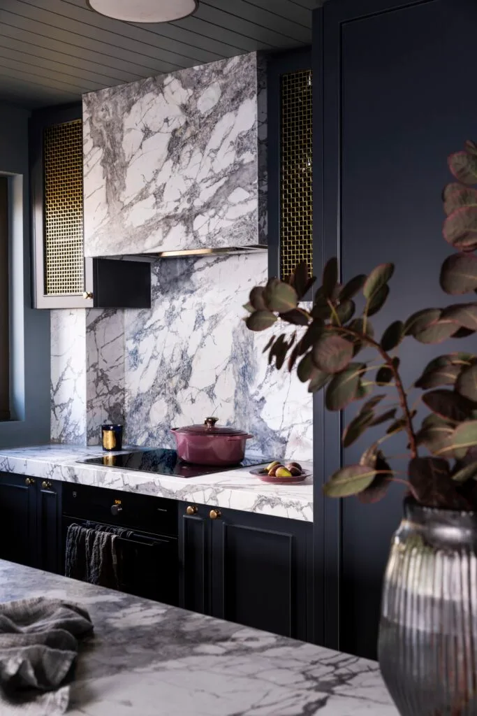 A dark teal kitchen with white marble benchtops and splashbacks.