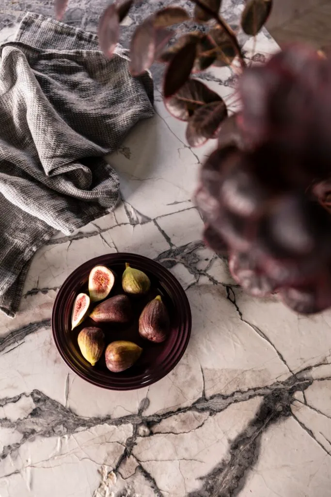 A bowl of figs sitting on a white and black marble benchtop.