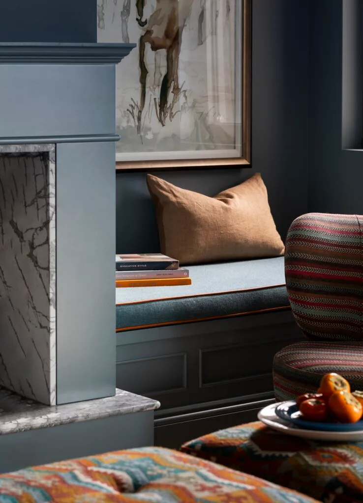 A bench nook with a pillow beside a marble fireplace.