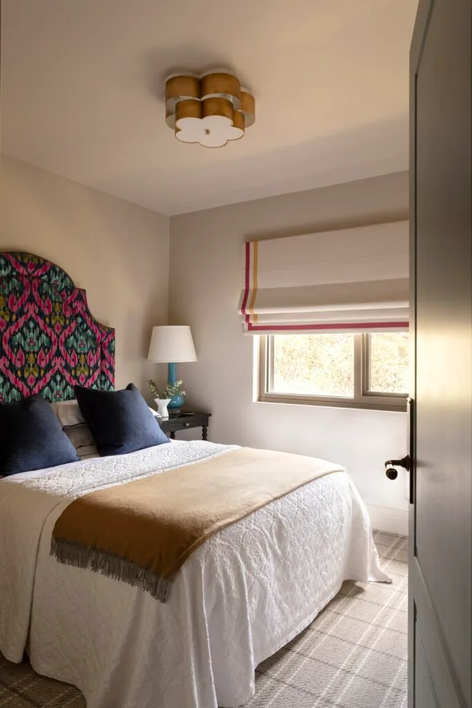 A main bedroom with a mixed patterned bedhead, flower-shaped lighting and white blinds.