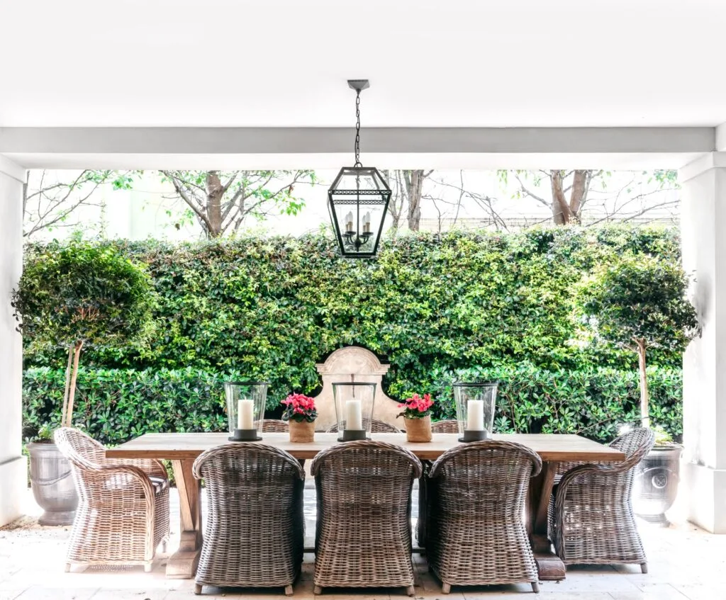 An outdoor alfresco area with rattan seating and green hedges.