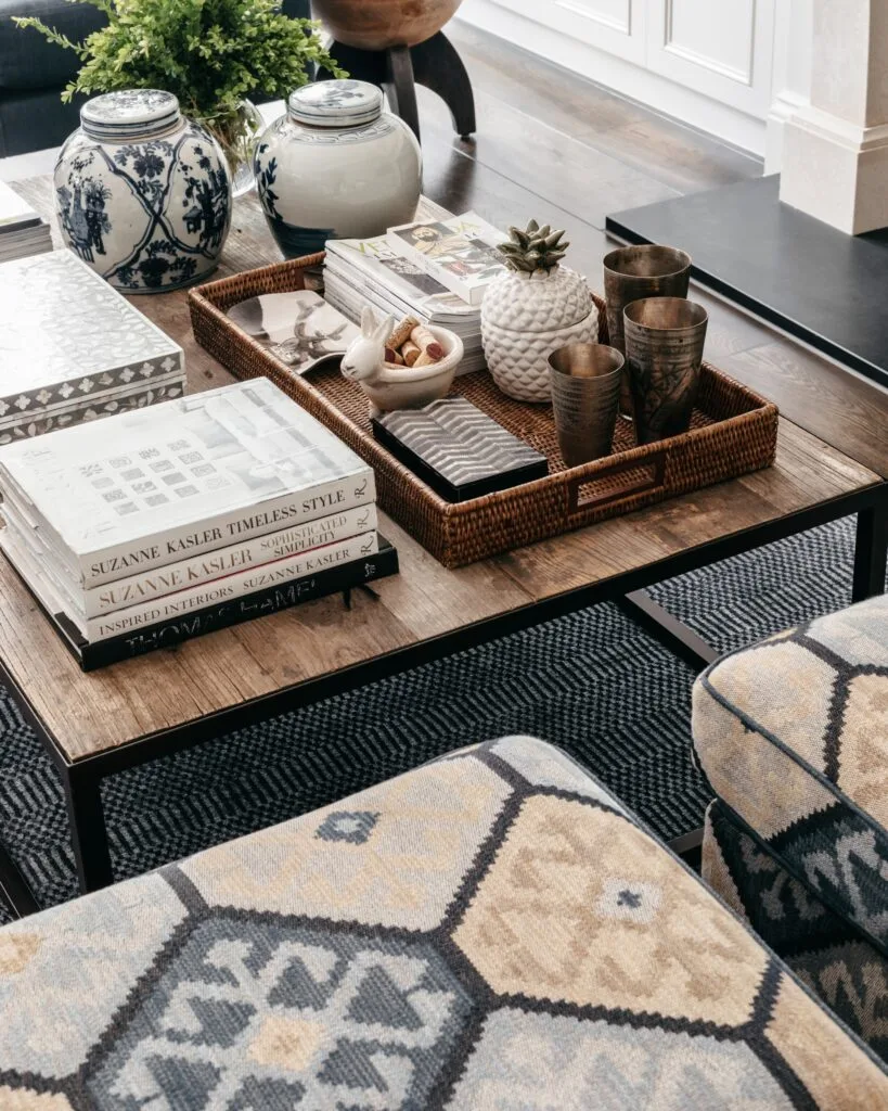 A timber coffee table with ceramic vessels, books and a rattan tray.