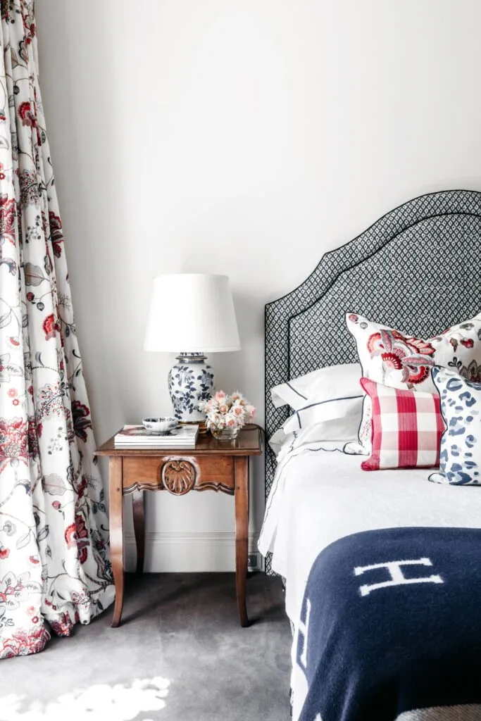 A guest bedroom with floral curtains, a timber side table and grey lined bedhead.