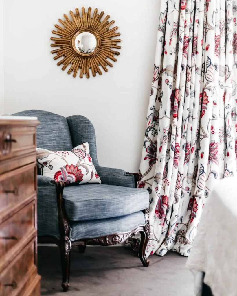 A blue vintage-style armchair beneath a decorative sun mirror.