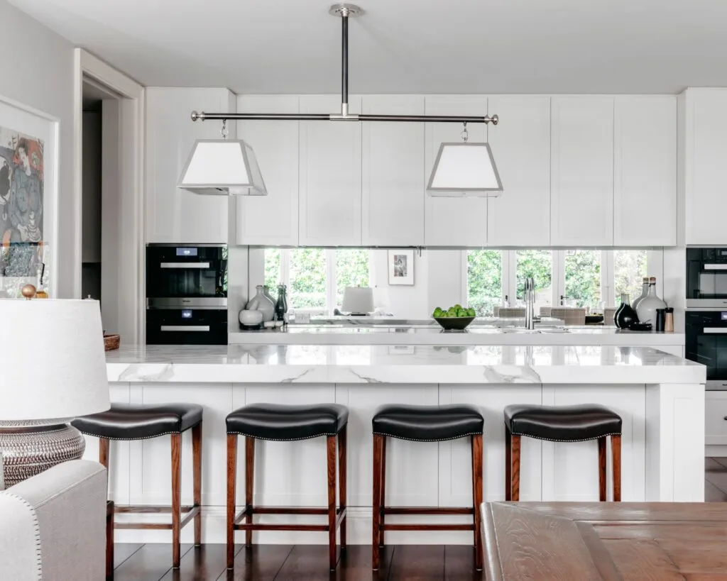 A classic white kitchen with a marble island and leather stools.