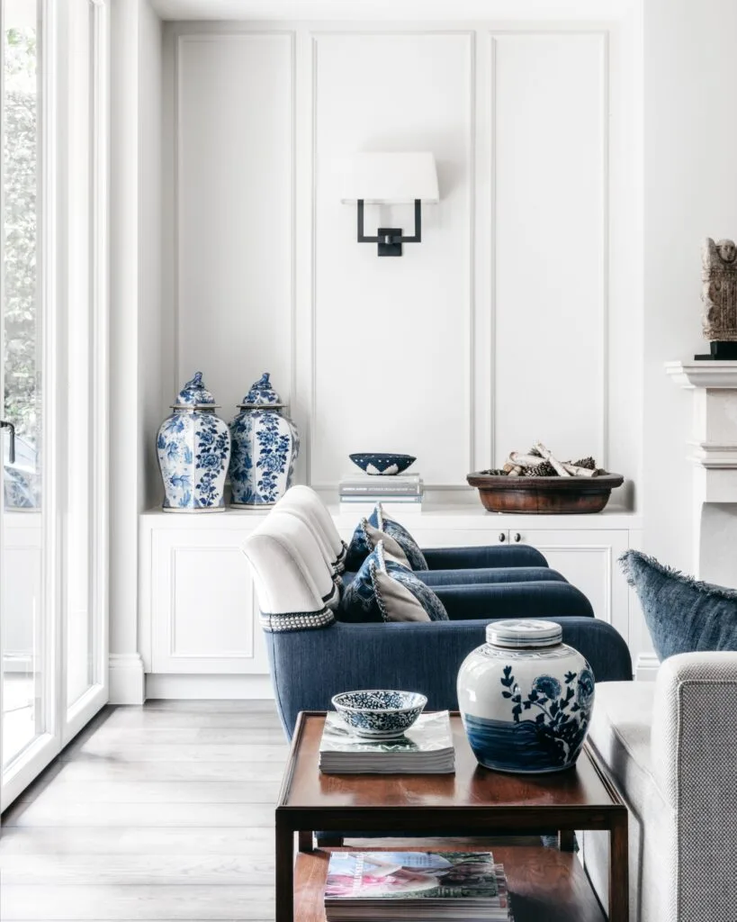 A formal style living room with wainscoting, ceramic pots and blue armchairs.