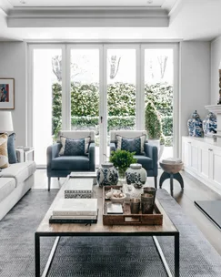 A formal style living area with blue armchairs, bifold glass doors and a timber coffee table.