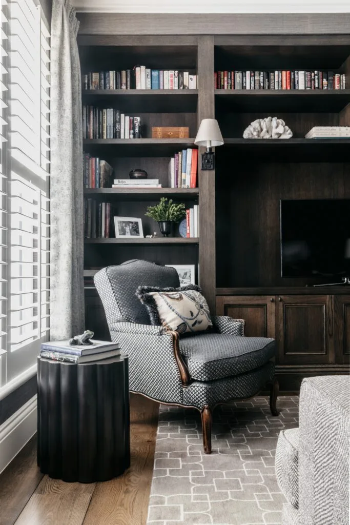 A study with timber in-built shelves and a grey patterned armchair.