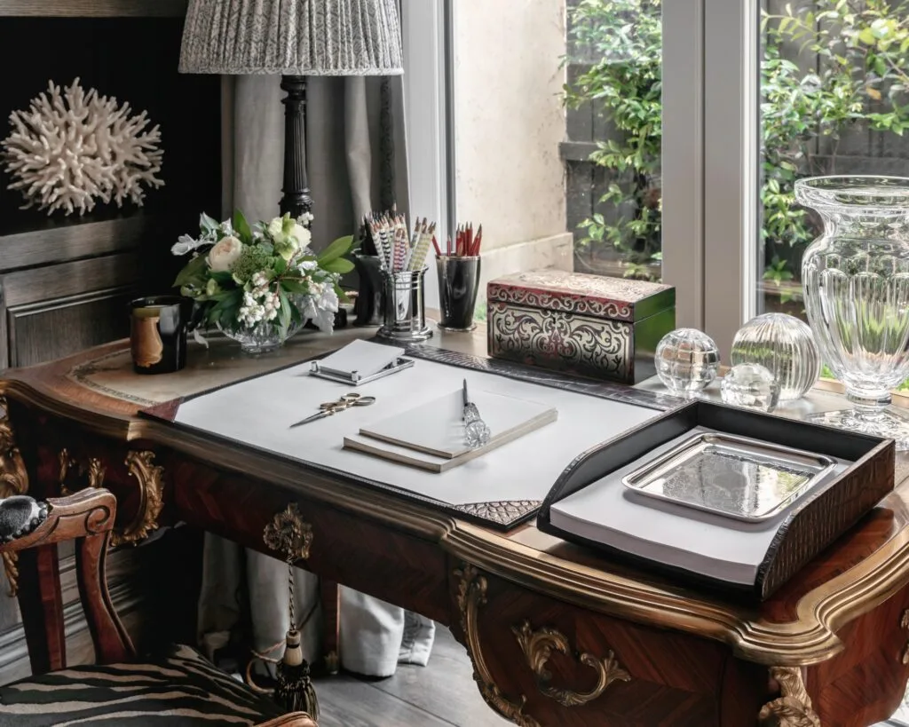 A classic timber writing desk with a paper organiser, glass vase and a lamp.