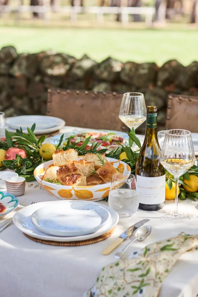 An outdoor tablescape with wine and a bowl of focaccia bread.