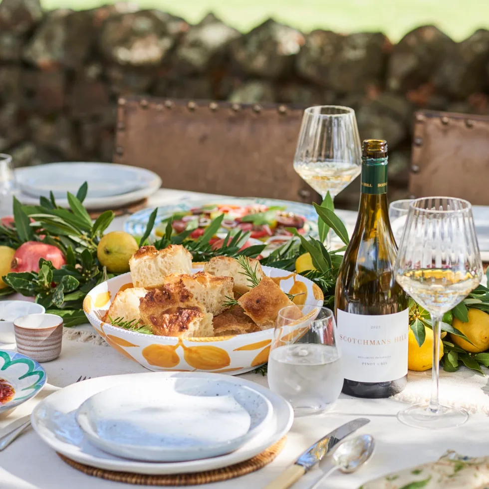 An outdoor tablescape with wine and a bowl of focaccia bread.