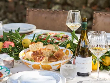 An outdoor tablescape with wine and a bowl of focaccia bread.