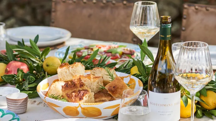 An outdoor tablescape with wine and a bowl of focaccia bread.