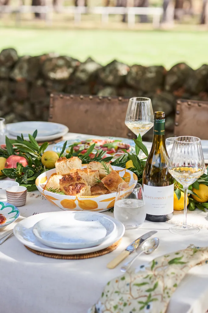An outdoor tablescape with wine and a bowl of focaccia bread.