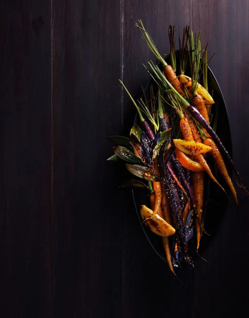 Gin and orange roasted carrots served on a table.