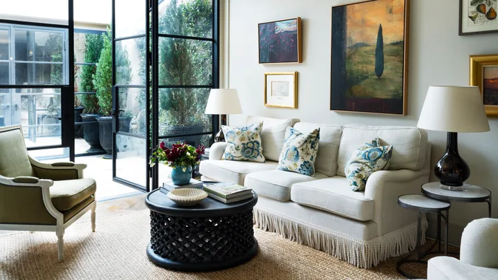 A living room with steel doors, landscape artworks and neutral furniture.