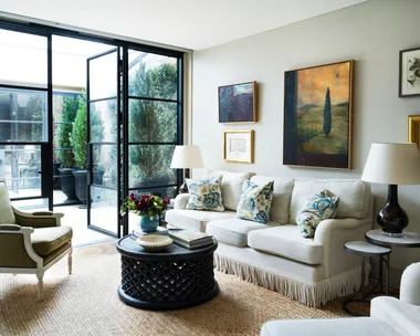 A living room with steel doors, landscape artworks and neutral furniture.