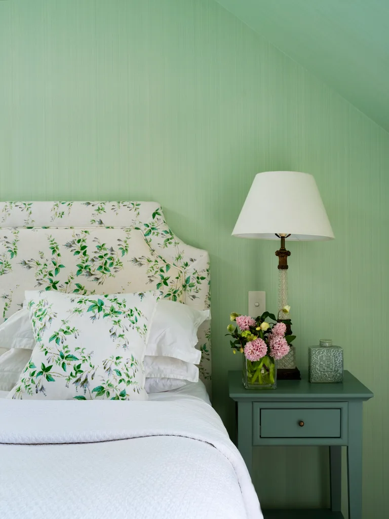 A pastel green main bedroom with a floral bedhead and vintage furniture.