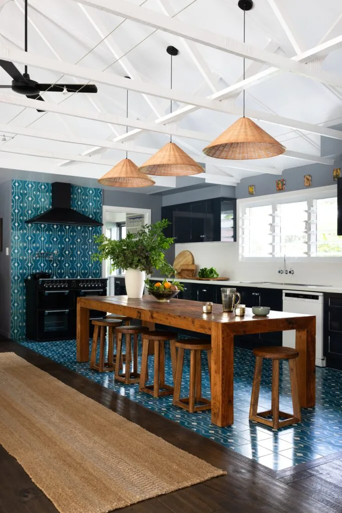 A European-style kitchen with blue mosaic tiles, a timber bench and rattan light pendants.