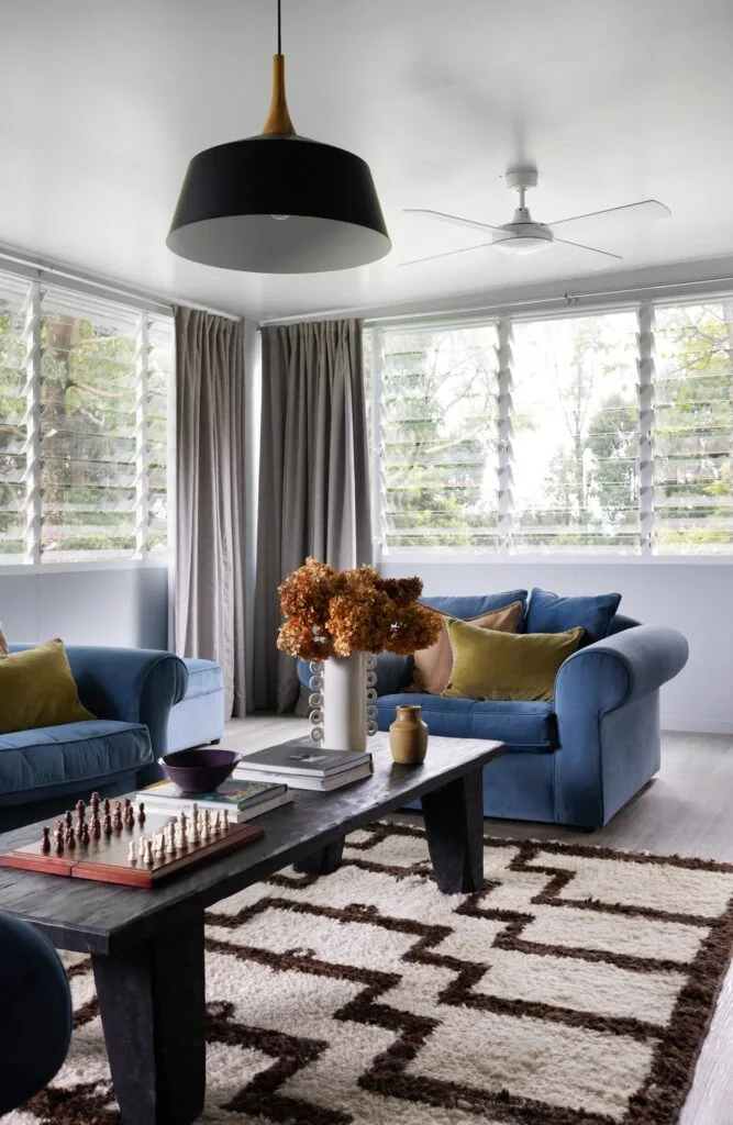 A sunroom with blue sofas, a long timber coffee table and a brown and white rug.