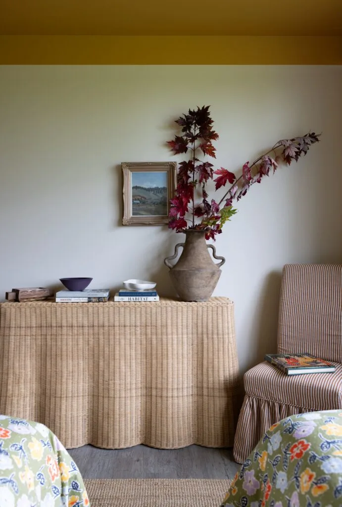 A wavy wicker console topped with books and a vintage vase.