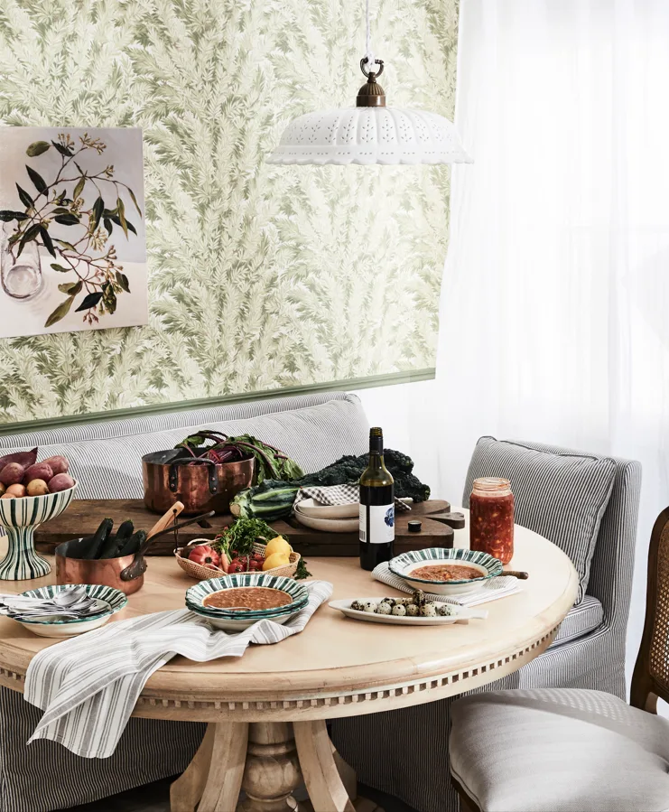 A round timber table is covered in handpainted bowls and plates while a bench and two chairs provide seating.