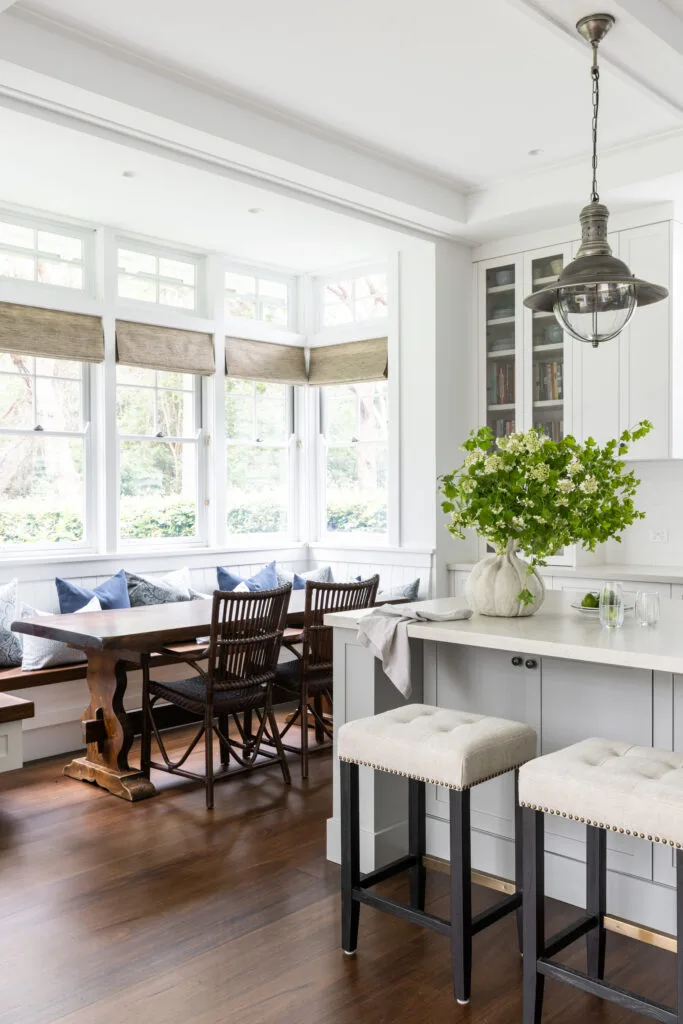 A built-in timber window seat, topped with white and blue cushions, provides seating around this breakfast nook, complete with rectangular table.