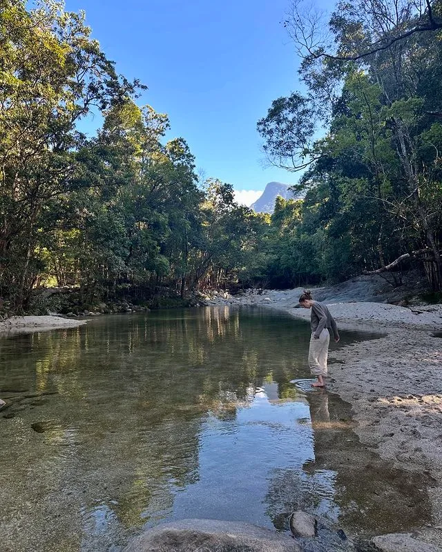 Phoebe Dynevor standing by the water in the rainforest.
