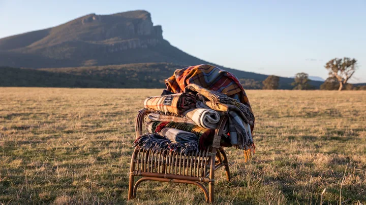 A stack of blankets on a cane chair with a mountain range in the distance.