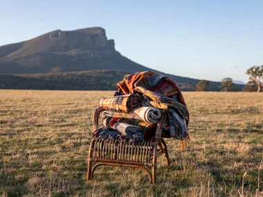 A stack of blankets on a cane chair with a mountain range in the distance.