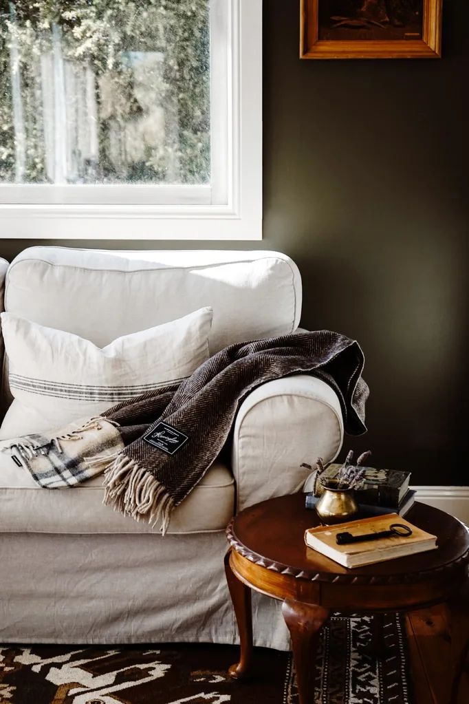 A cosy woollen blanket laying on a white armchair below a window.