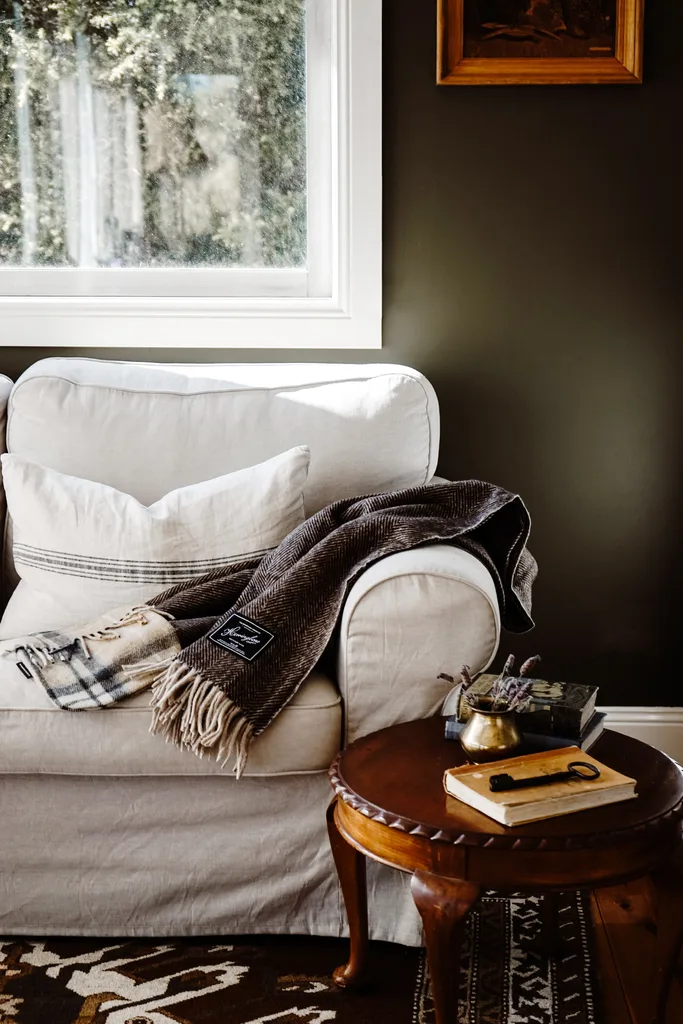 A cosy woollen blanket laying on a white armchair below a window.
