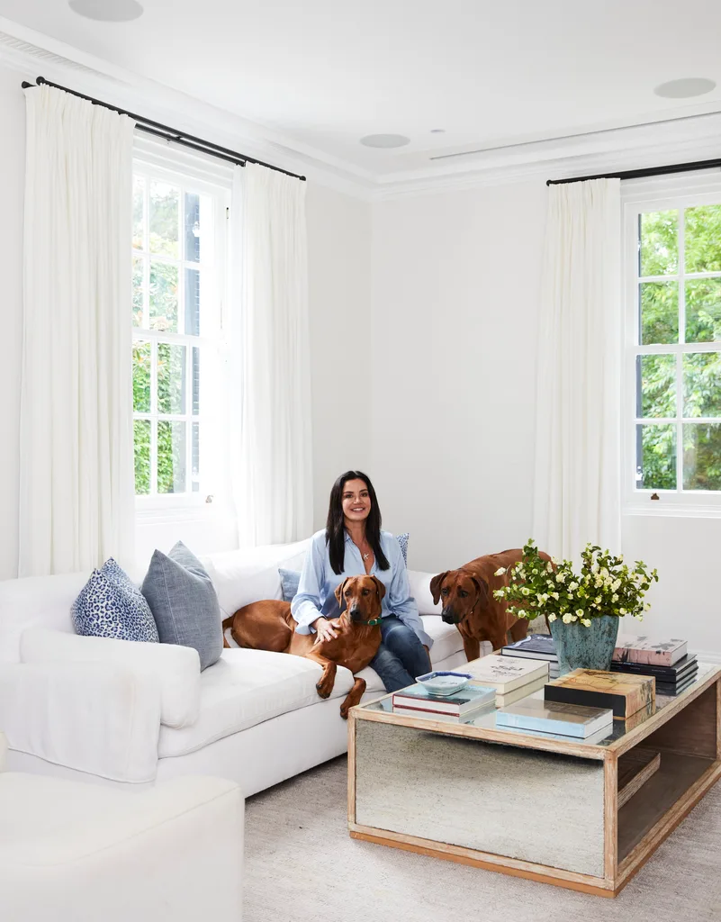 Krissy Marsh and her dog sitting on a sofa in the all-white living room.