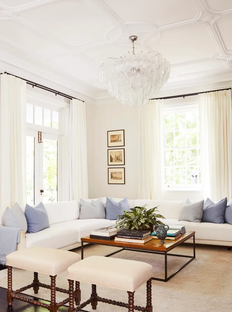 A classic white living room with a chandelier and L-shaped sofa.