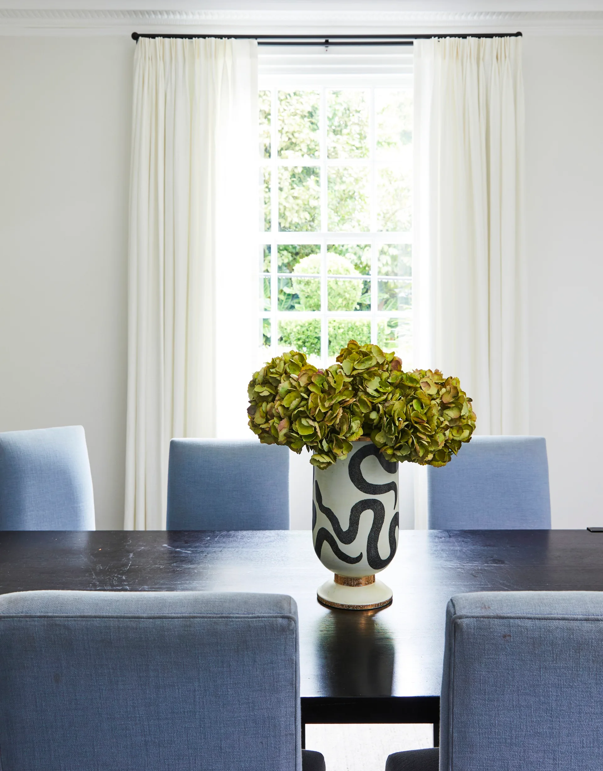 An abstract painted vase sitting on a timber dining table.