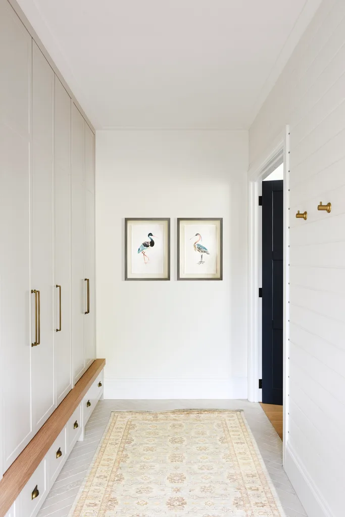 A bright white mudroom with a vintage-style rug runner.