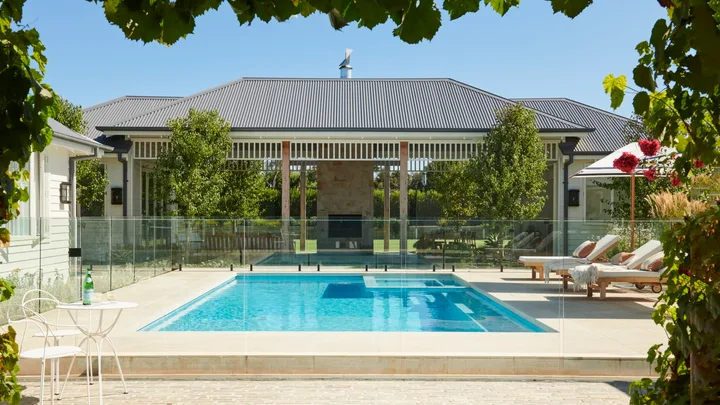 An outdoor pool area with white loungers leading to an alfresco area.