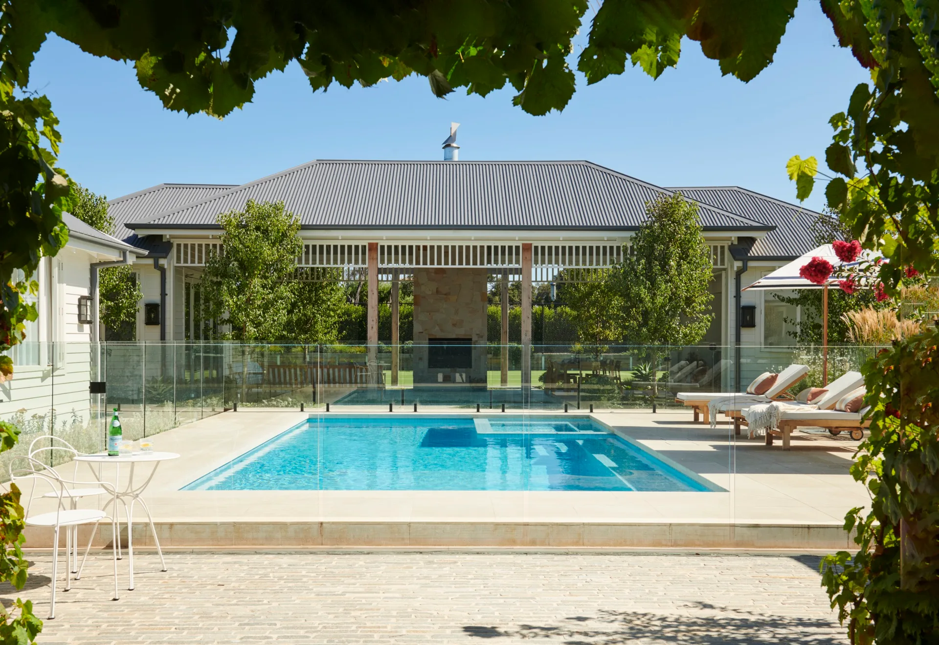 An outdoor pool area with white loungers leading to an alfresco area.