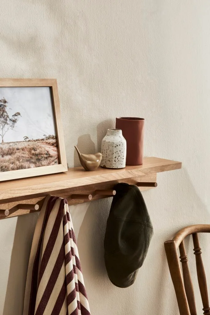 A timber coat rack with a landscape artwork and ceramic vessels on top.